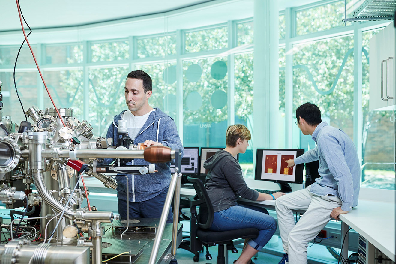 A man working on quantum equipment in a laboratory while a man and woman look at a computer screen