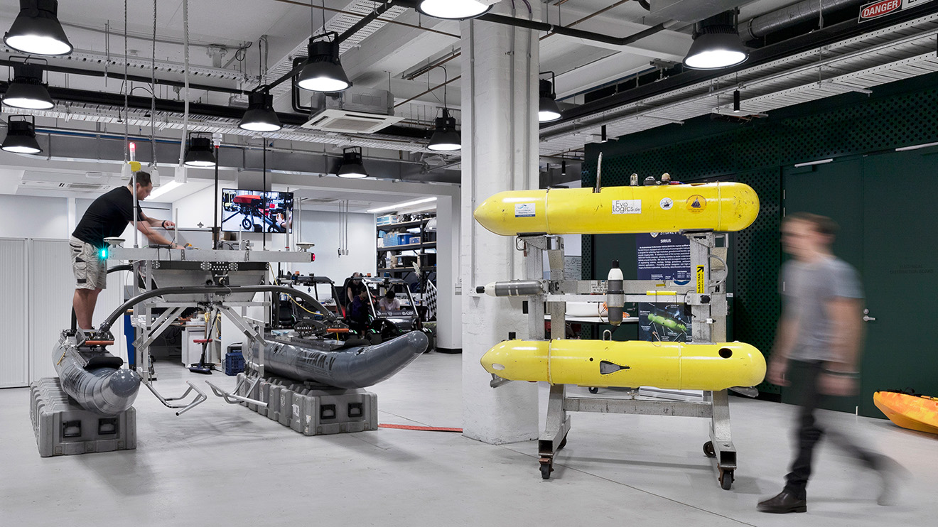 A robotics lab with two staff working at the Australian Centre for Robotics, showing different kinds of robotic machinery.