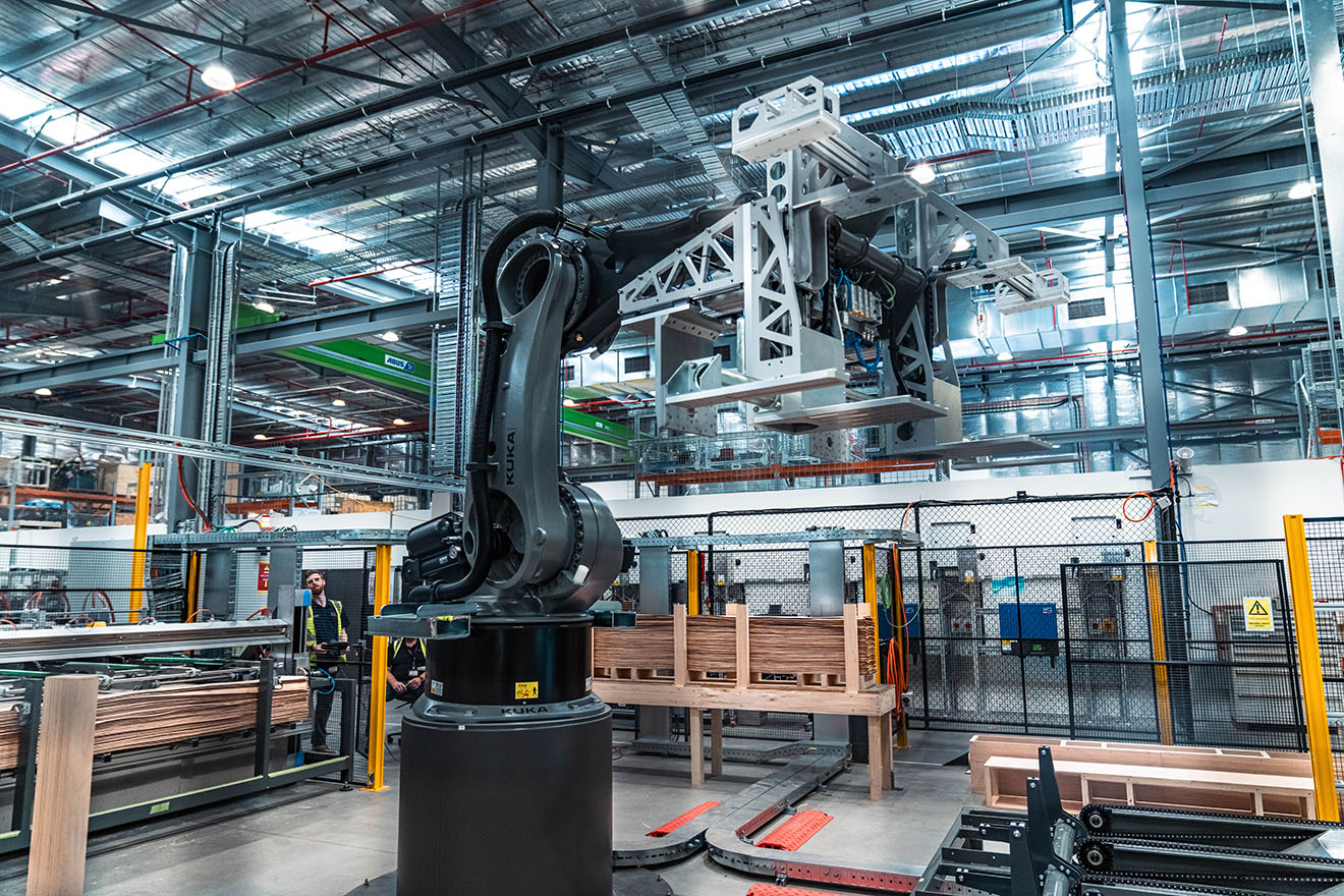 A large grey robot in a warehouse, operated by a staff member with a remote control.