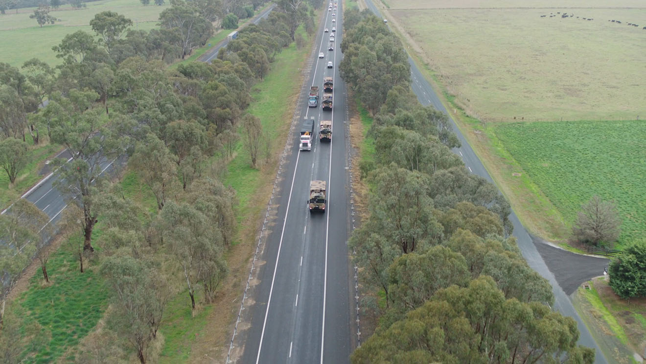 A line of vehicles driving down a highway between strips of Australian vegetation.