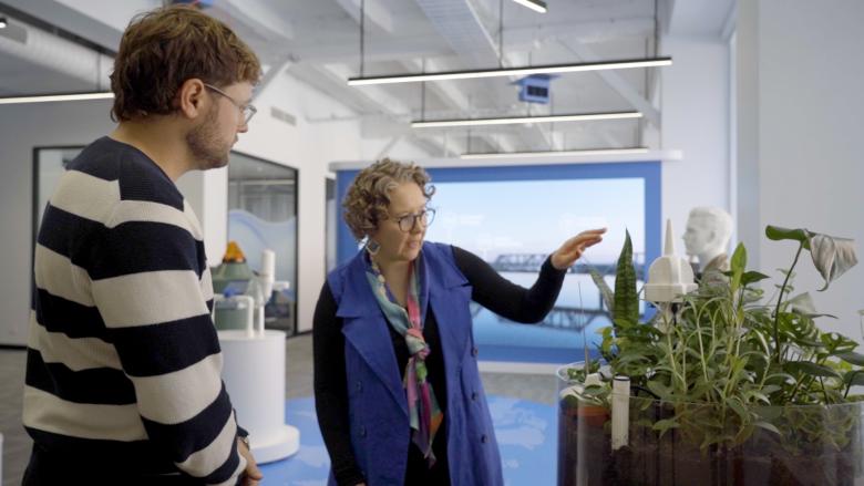 Inside a white display room, two people look at a plant sensor which has been placed inside a small round garden bed. 