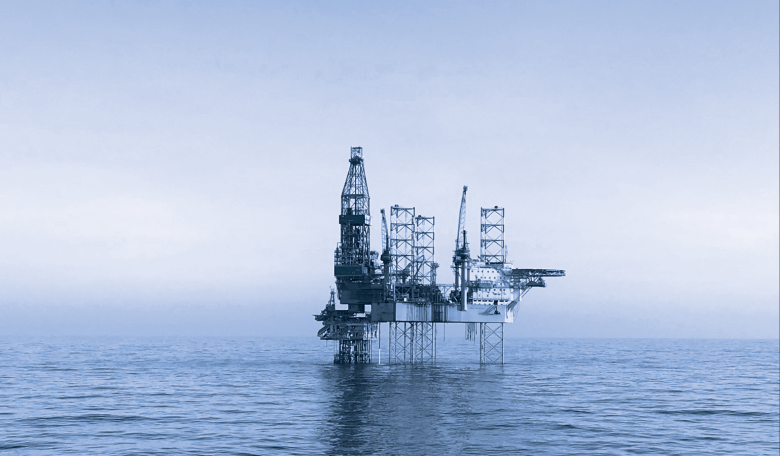 Image of an oil rig in the middle of the ocean. The image has a blue tint.