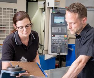 A man and women standing in a workshop, reviewing notes on a clipboard. 