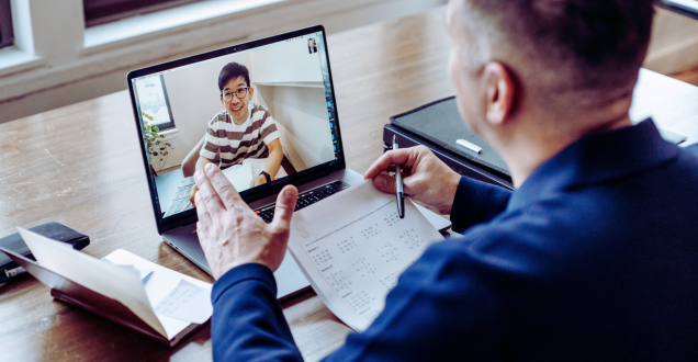 Man at desk talks to another man via video conferencing 