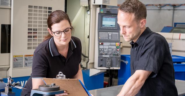 A man and women standing in a workshop, reviewing notes on a clipboard. 