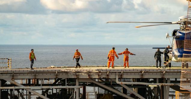Crew members board and monitor a helicopter on a helideck offshore
