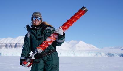 Female polar marine biologist stands in a snowy landscape holding an oversized drill bit