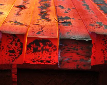 Close up image of metal billets, glowing red from casting. 