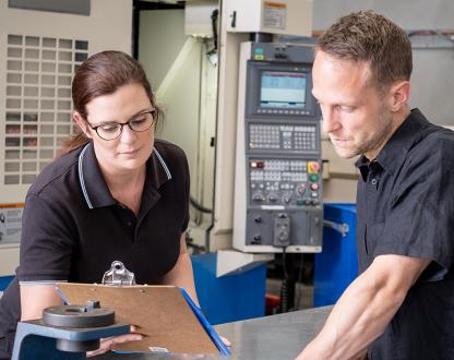 A man and women standing in a workshop, reviewing notes on a clipboard. 