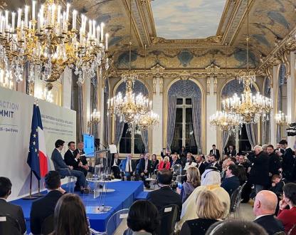 Photo of the AI Action Summit stage located in the Grand Palais. Several political figures are sitting down and talking to a room filled with people. 